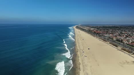 Vista-Aérea-De-Huntington-Beach,-California,-Mirando-El-Tráfico-En-PCH-Y-Algunas-Olas-Grandes-Rompiendo-En-La-Orilla.