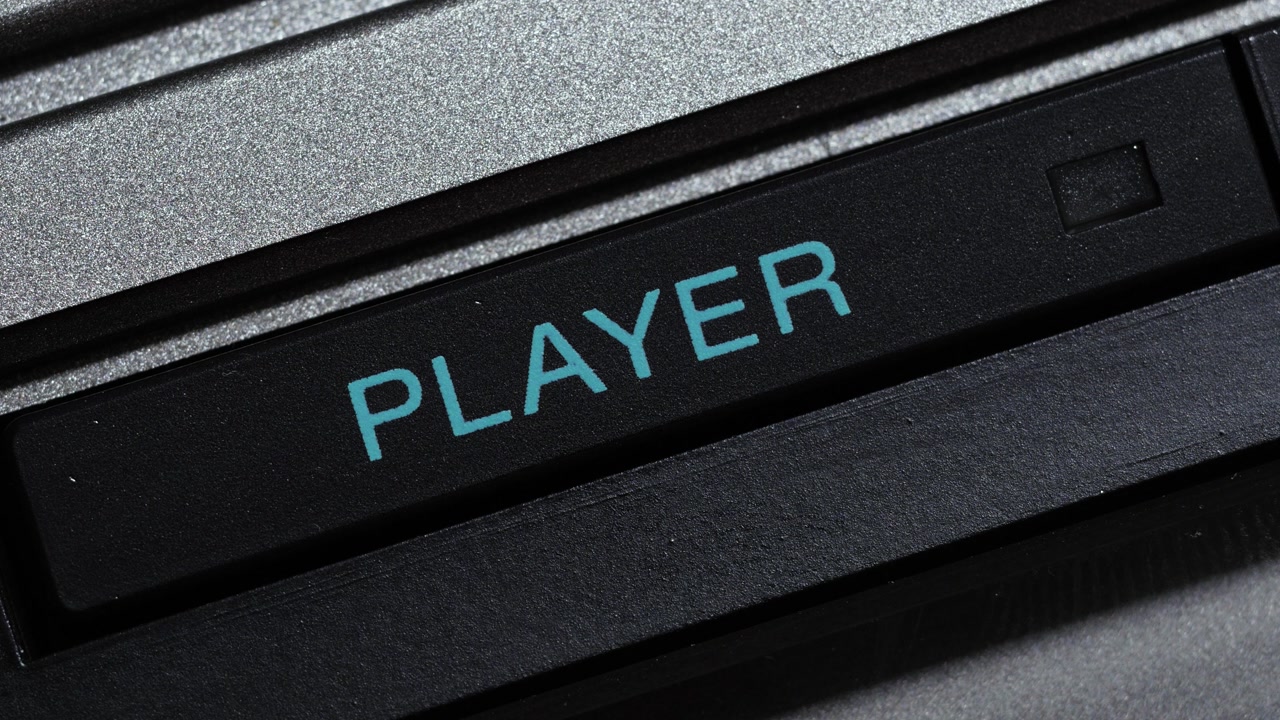Black player button with blue text being pressed in macro close up