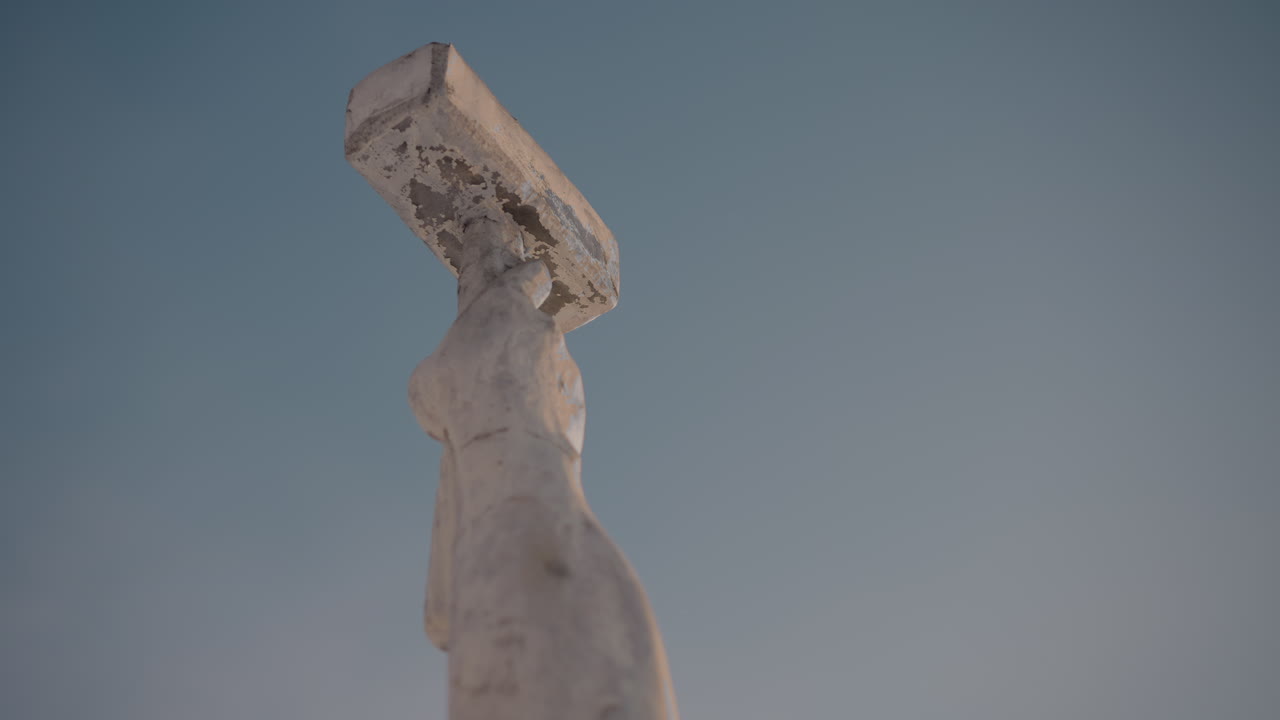 Low angle close up of weathered sculpture reaching into bright blue sky, emphasizing texture and shape against clear daylight background with no visible surroundings