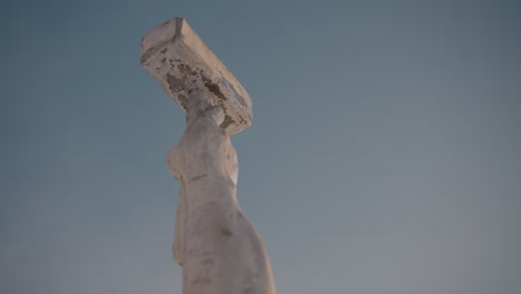 low angle close up of weathered sculpture reaching into bright blue sky, emphasizing texture and shape against clear daylight background with no visible surroundings