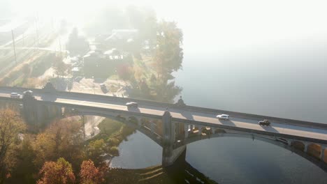 cinematic aerial of car traffic on bridge over river during dramatic morning light and fog