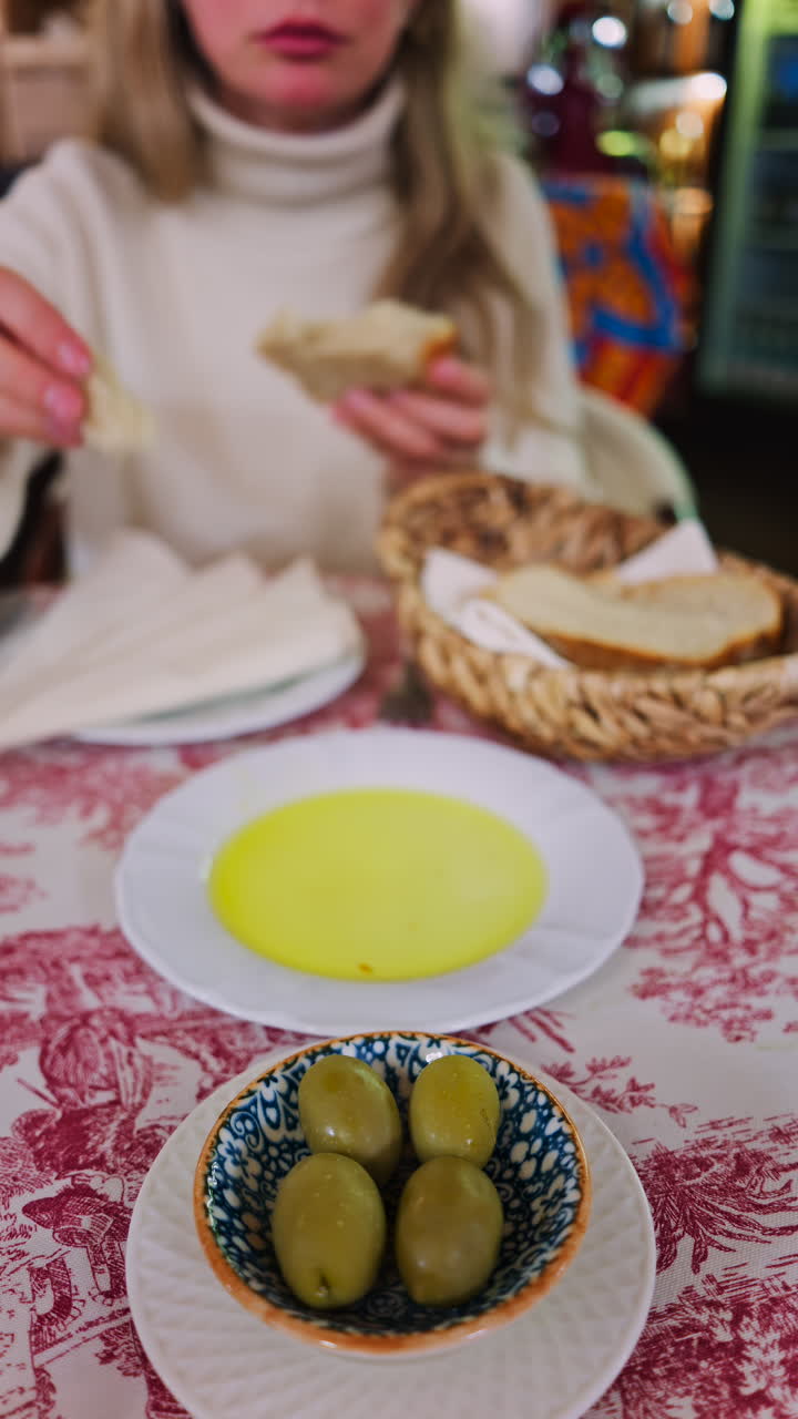 Close up of a woman dipping bread in olive oil and eating it at a restaurant. Vertical