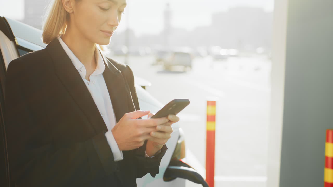 деловая женщина использует смартфон на зарядной станции для электромобилей