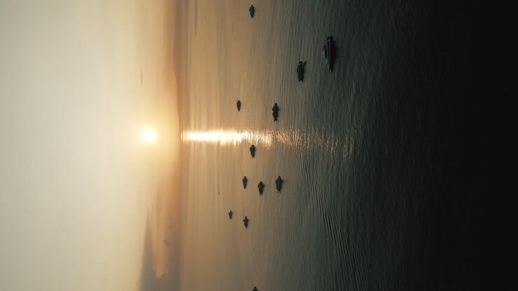 Inquadratura verticale di un'alba a Bali, ripresa aerea con drone del sole che sorge, riflesso in un mare calmo, barche che galleggiano nell'oceano