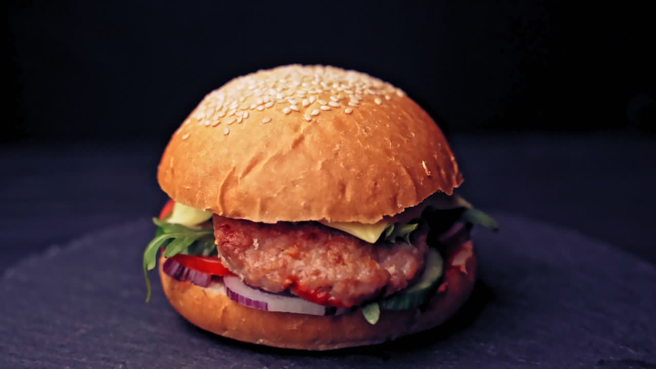 Great Burger with beef cutlets, tomatoes, lettuce with melted cheese rotates on a wooden Board on black background.