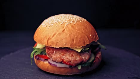 great burger with beef cutlets, tomatoes, lettuce with melted cheese rotates on a wooden board on black background.