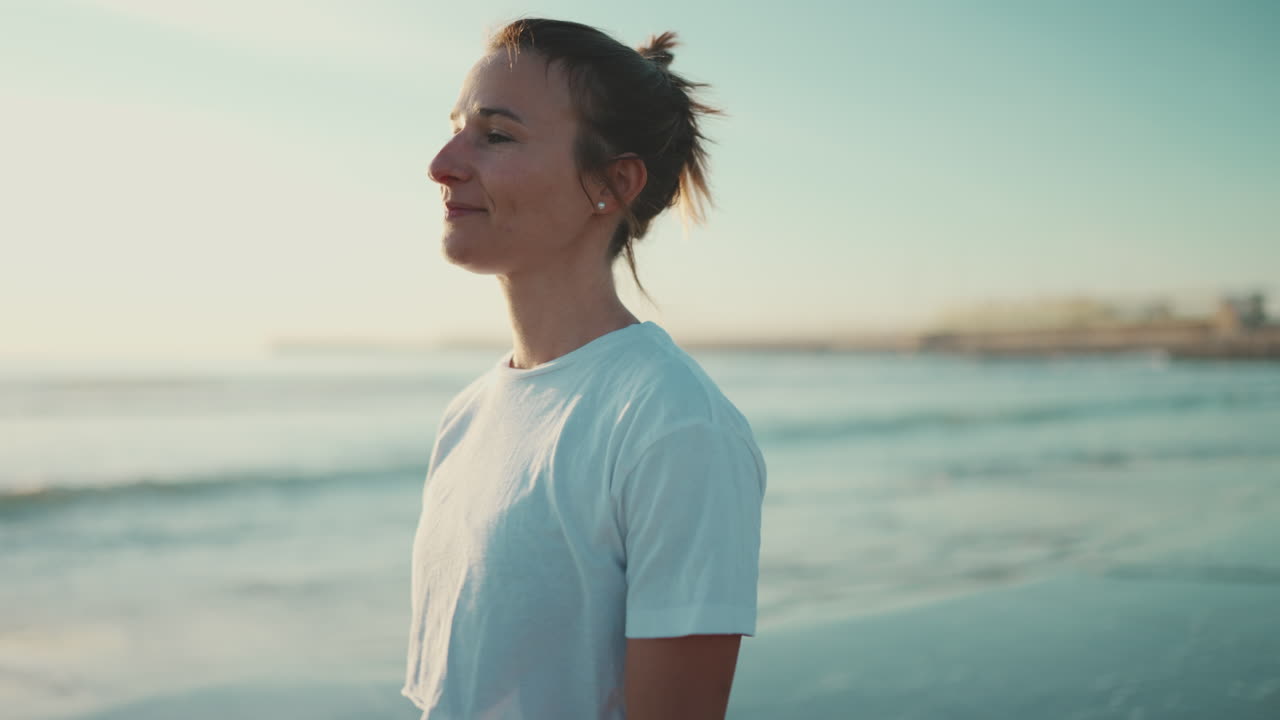 Blonde woman looking happy walking along the sea after yoga practice.