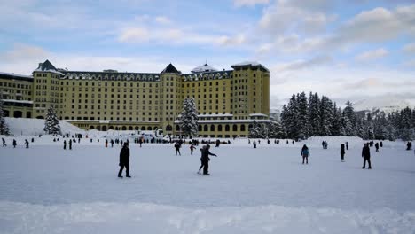 People  Ice Skating In The Frozen Lake Louise Located In Front Of Luxury Resort Of Fairmont Chateau Lake Louise. wide shot