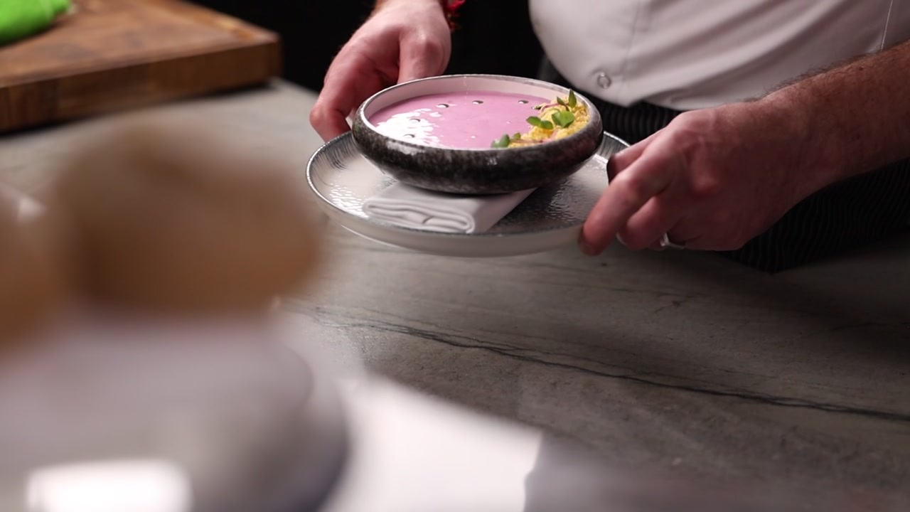 Chef Presenting a Bowl of Creamy Pink Soup in a Restaurant Kitchen