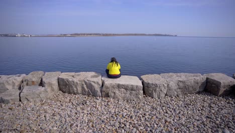 persona en el parque trillium de toronto con auriculares sentados cerca del lago con una chaqueta amarilla brillante durante el día