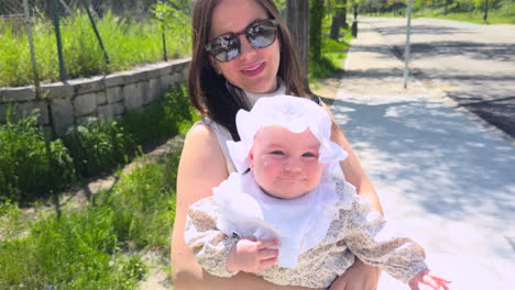 close-up of a happy woman holding her daughter in her arms while smiling under the sunlight on a peaceful path surrounded by nature