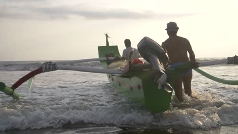 men pushing indonesian outrigger into ocean