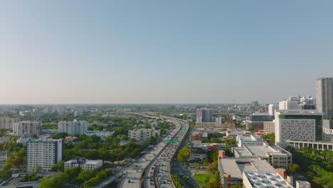 Aerial-ascending-footage-of-busy-multilane-highway-in-large-city.-Late-afternoon-shot-of-transport-infrastructure-in-town-in-flat-landscape.-Miami,-USA