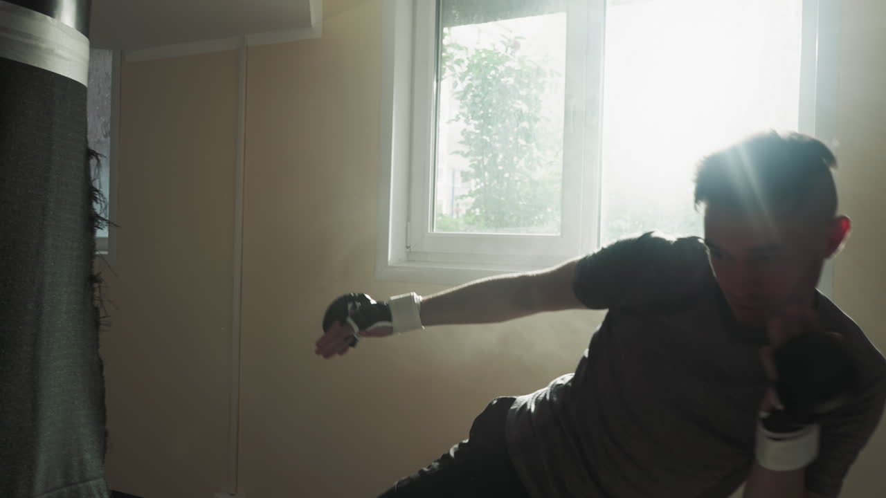 atleta ataca la bolsa de boxeo con los puños y la pierna en un club deportivo. joven kickboxer patea y golpea equipos pesados en el gimnasio a la luz del sol en cámara lenta