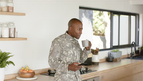 military man in kitchen holding smartphone and drinking coffee, looking thoughtful