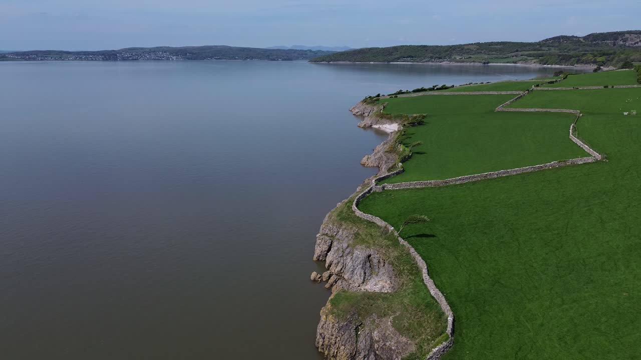 Coastal farming meadow aerial view establishing curving stone wall following Morecambe bay