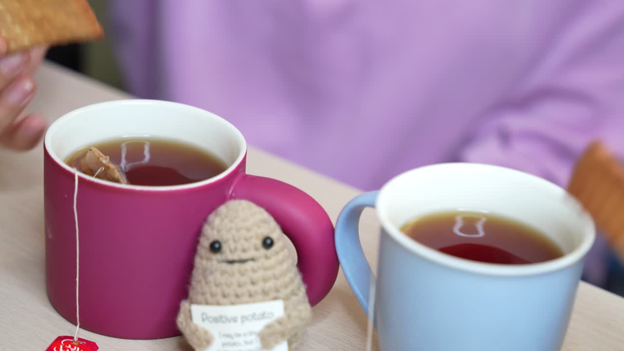 Close-up of two mugs of tea with biscuits being dipped, featuring a handmade "Positive Potato" plush toy. Cozy, playful, and perfect for lifestyle or comfort content