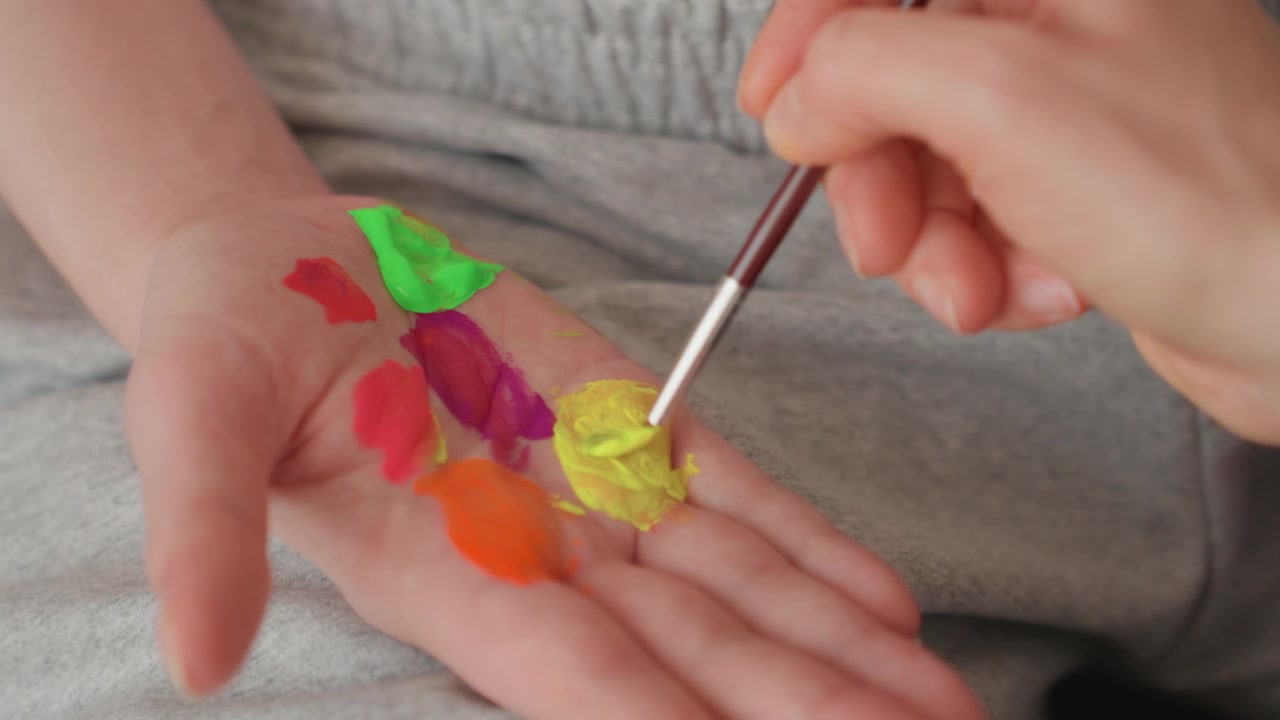 Close-up de mão misturando cores vibrantes de tinta na palma da mão com pincel