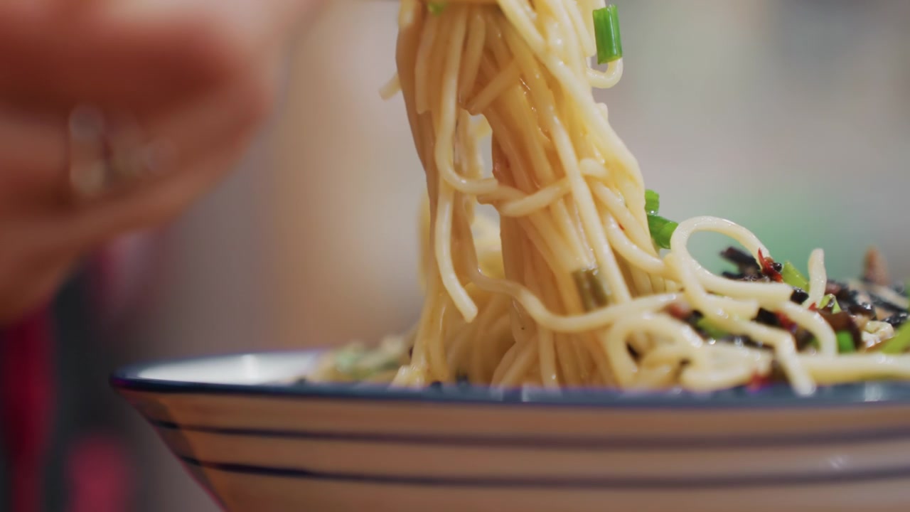 丼から箸で麺をすくい上げるクローズアップ。つややかな麺の質感、ネギと海苔の周りから立ち上る湯気。勢いよく麺をすすり、絡まった麺を操る手。映画のようなカジュアルな食事風景。