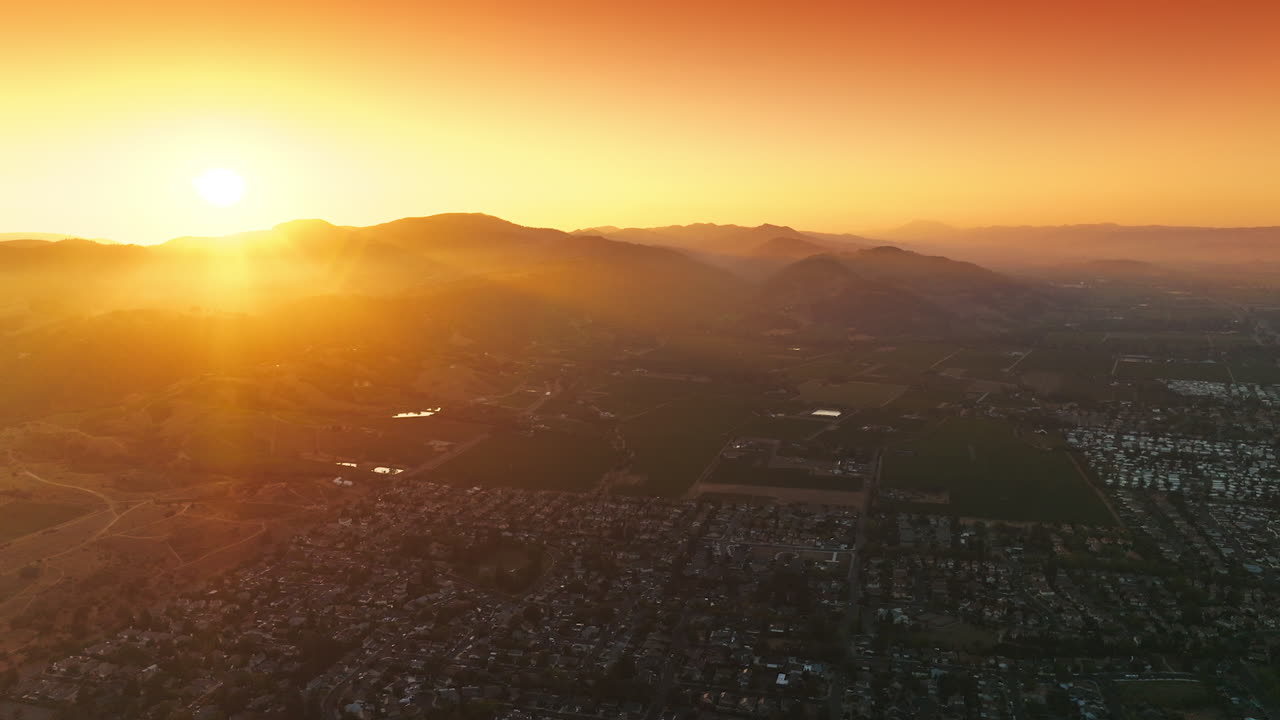 City with densely built architecture of low houses at sunset. Bright sun hiding behind the mountains. Aerial perspective.