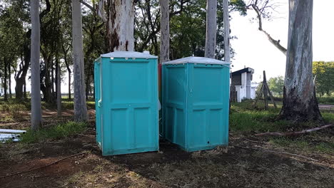 travelling out of gender-neutral aqua green blue portable bathrooms, in a park with forest