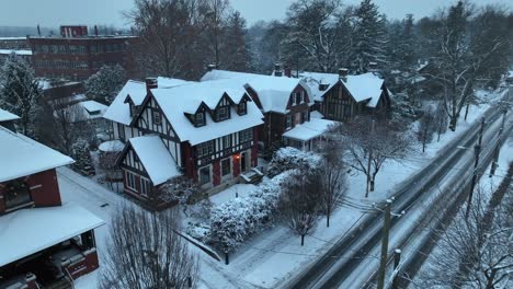 snowy tudor-style houses with steep gabled roofs, situated along a snow-lined street with bare trees