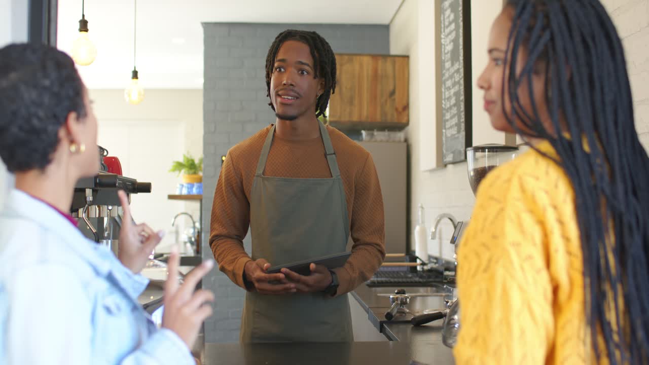 Female friends approaching cafe counter placing order while barista tapping tablet confirming order