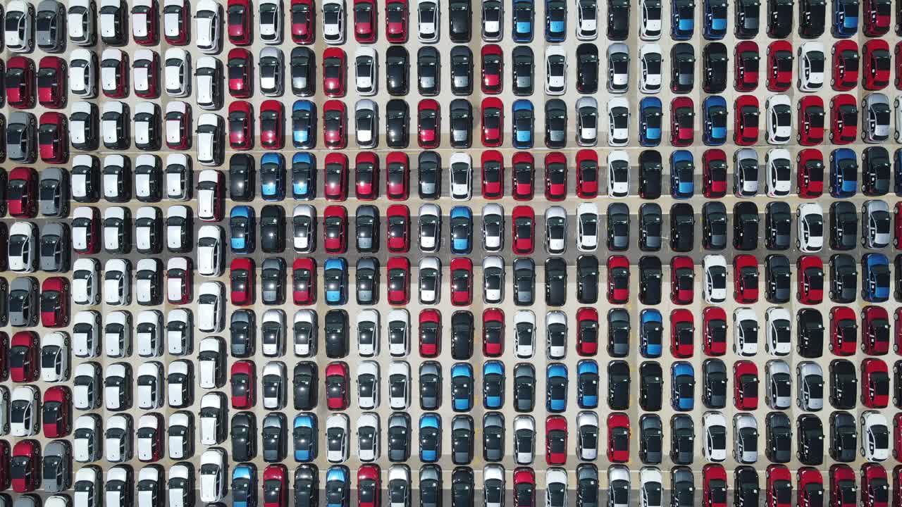 Aerial view of hundreds of cars neatly arranged by color in a distribution yard.