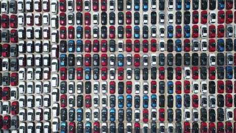 aerial view of hundreds of cars neatly arranged by color in a distribution yard.