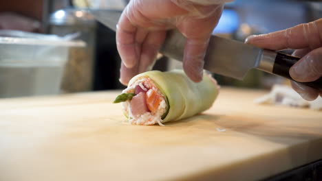 chef cortando maki de sushi, chef de sushi rebanando rollo de sushi envuelto en pepino con cuchillo, cámara lenta hd