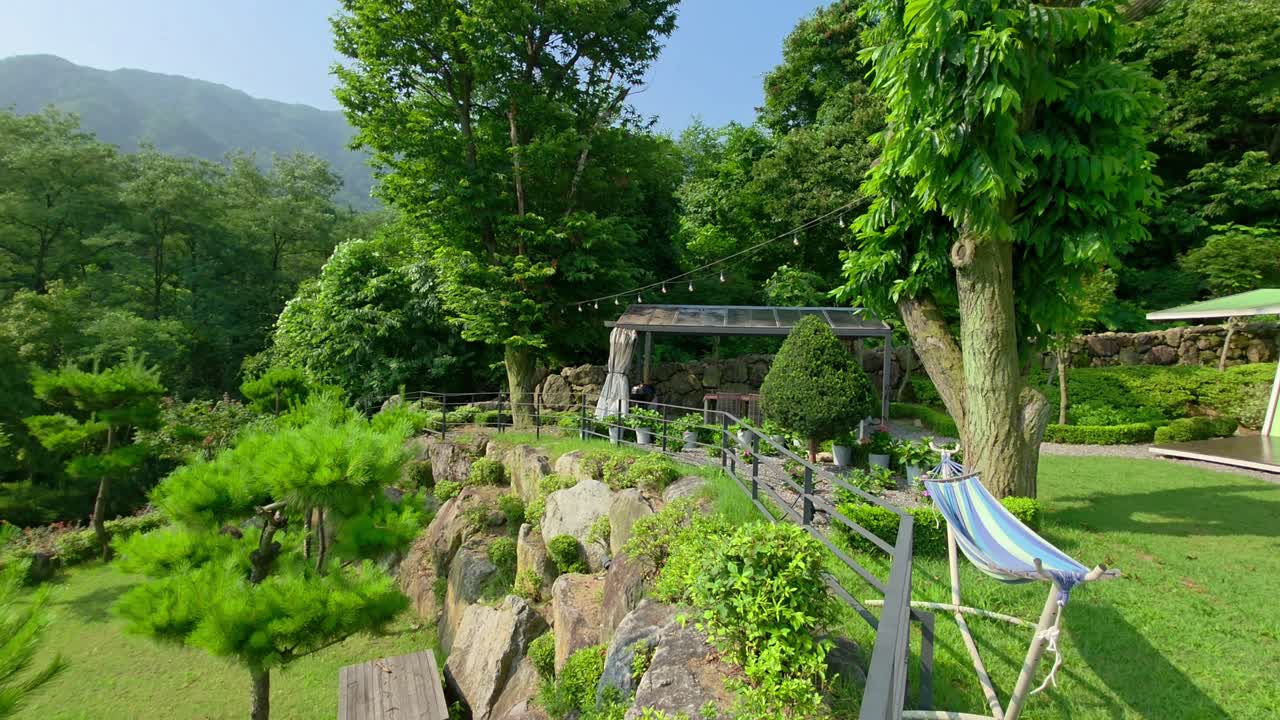 A smooth leftward pan reveals a serene mountain landscape, lush garden, and modern glamping site at Glam Free Resort in Gapyeong, Korea