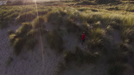 drone shot of young boy on beach vacation playing in sand dunes against flaring sun