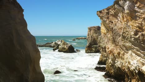 the sea rushes in between two cliffs along a rocky coast in southern california - pull back slow motion