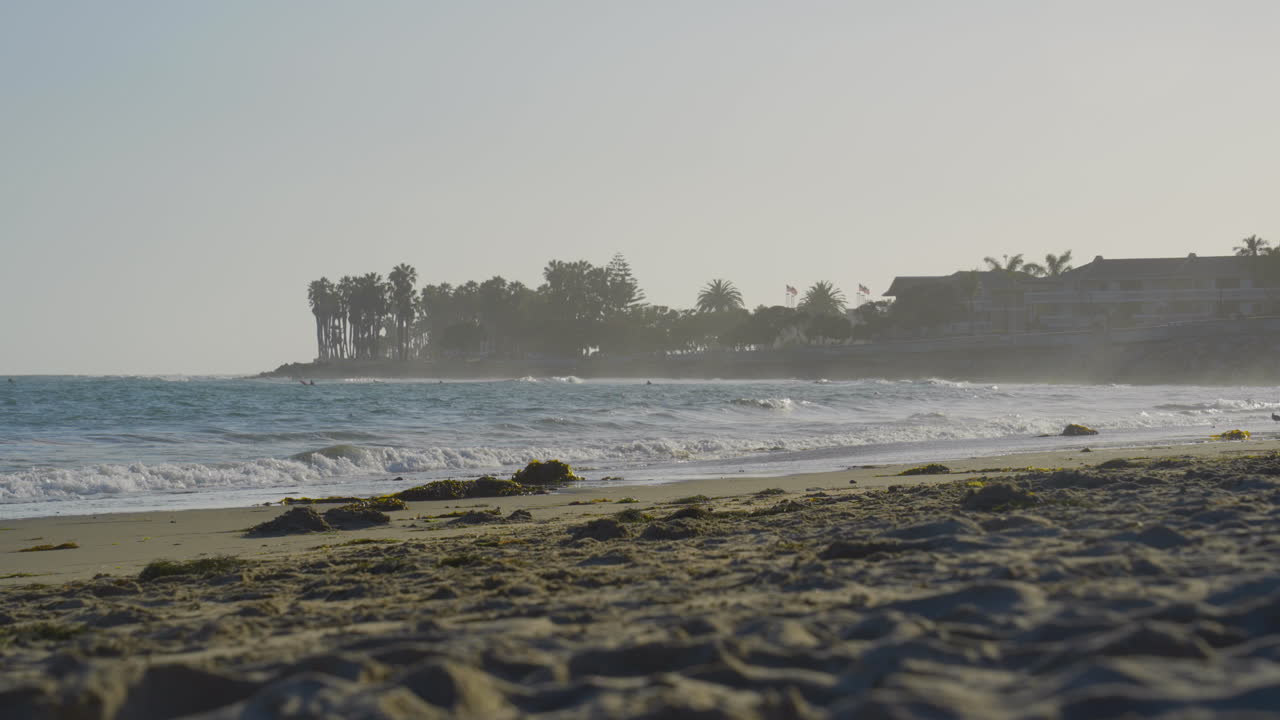 toma estacionaria de una ola que se estrella contra las costas de la playa de ventura en una mañana nublada con una gaviota volando a través del marco al final