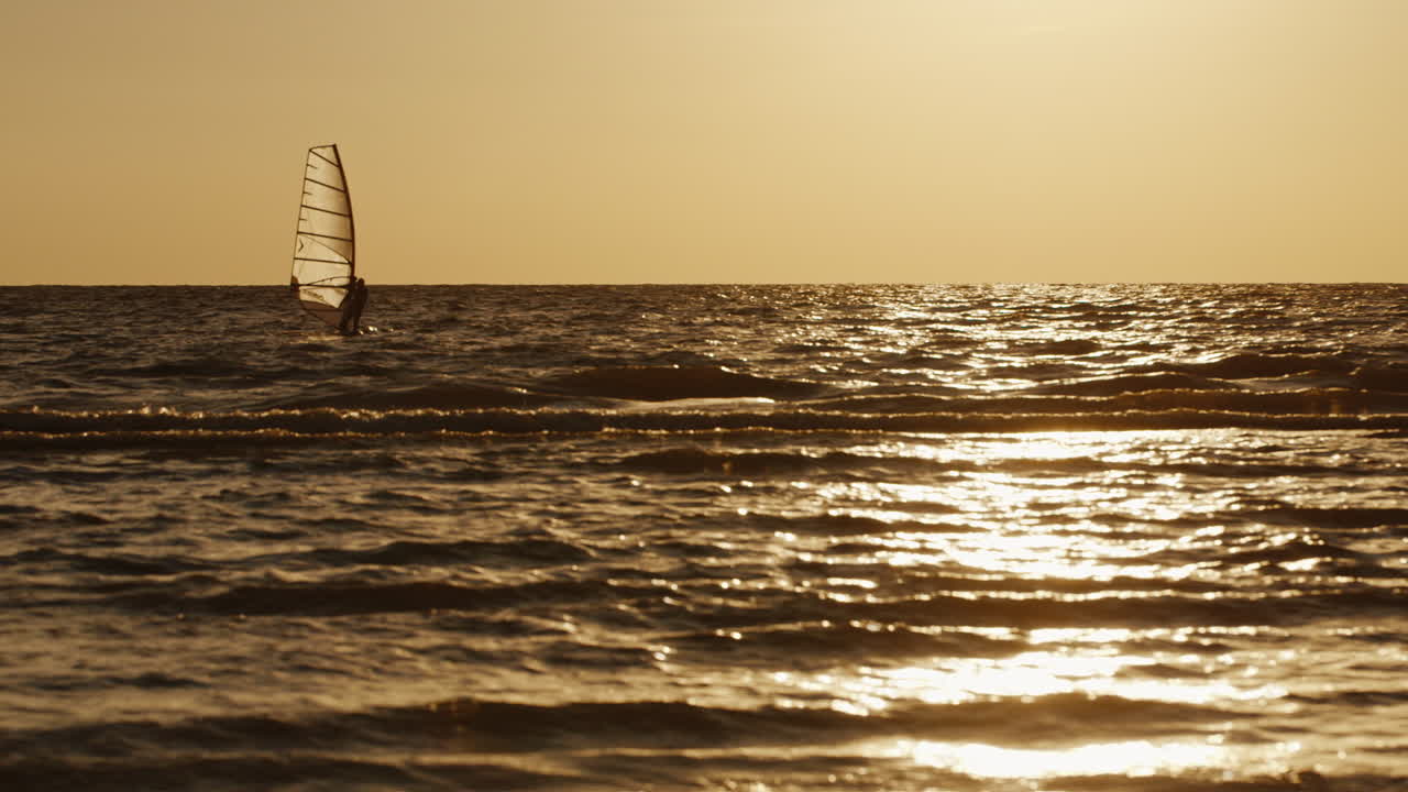windsurfista flota en una tabla con una vela al atardecer