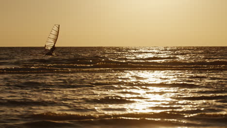 Windsurfer-Schwimmt-Auf-Einem-Brett-Mit-Segel-Bei-Sonnenuntergang