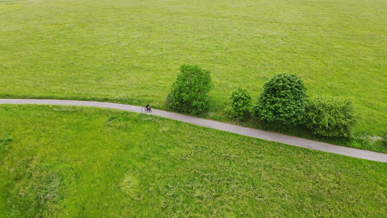 Solitary cyclist rides through remote green pastures, Czech bikepacking journey