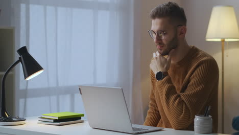 adult caucasian man is viewing video on display of notebook sitting in living room using internet for education and entertainment male portrait in home