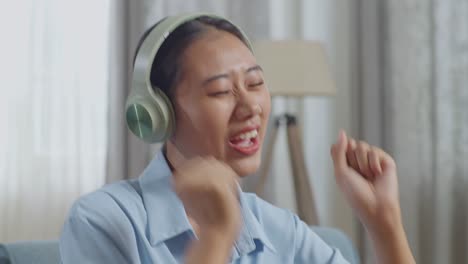 거실 의 소파 에 앉아 음악 을 듣고 춤 을 추는 헤드폰 을 착용 한 아시아인 여자 의 근접 사진