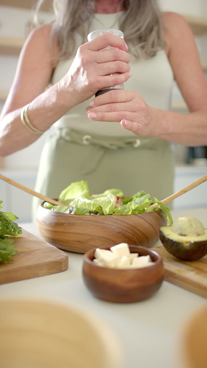 Vertical video: Seasoning fresh salad, woman preparing healthy meal in home kitchen