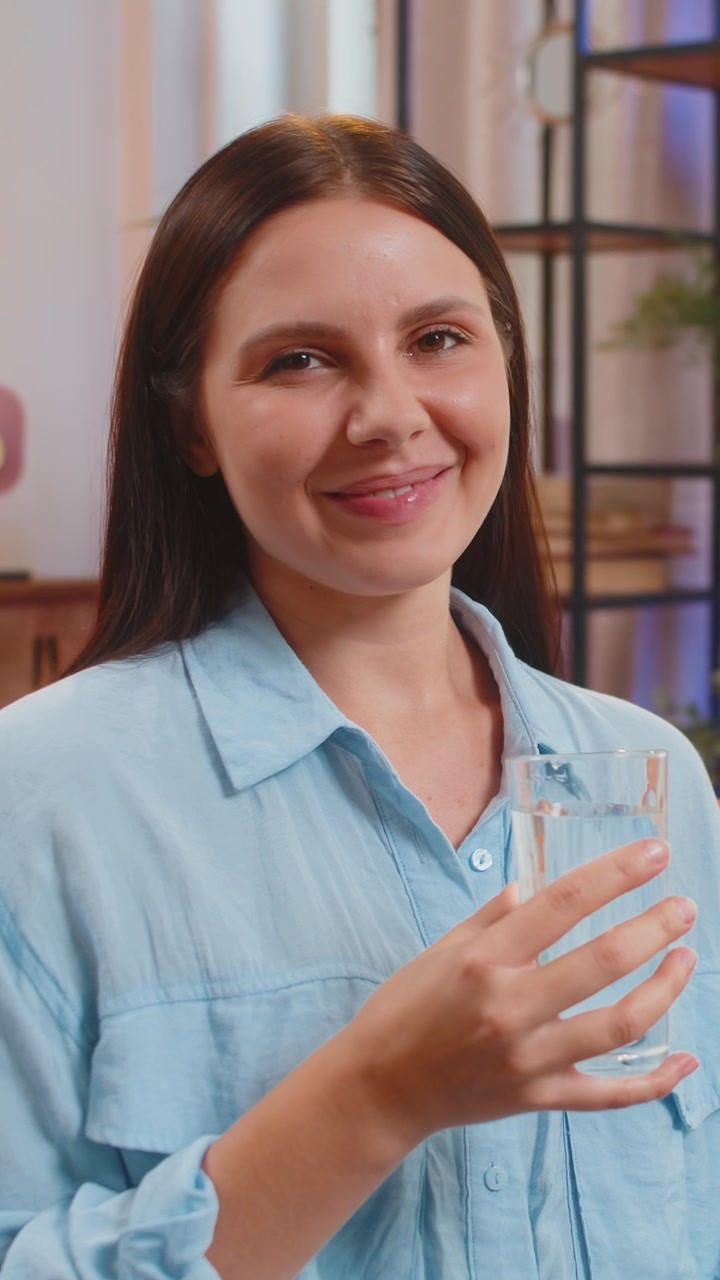 Giovane donna assetata si siede a casa tenendo un bicchiere di acqua naturale fare sorsi bere acqua filtrata