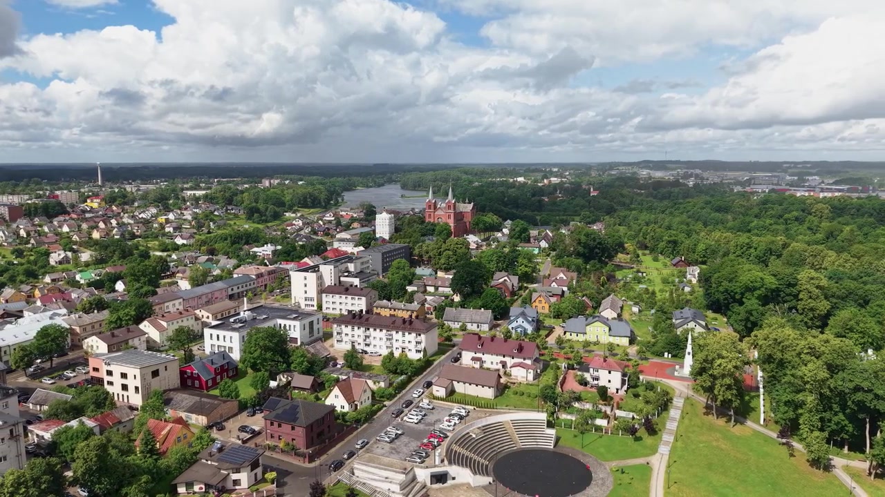 Dynamiske droneoptagelser viser Plungė, Litauen, med farverige hustage, naturskønt parklandskab, dramatiske skyer og den ikoniske røde kirke, der blander bycharme med naturlig skønhed i skarpt dagslys.