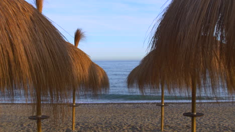 Tiro-De-Cardán-De-4k-Deslizándose-A-Través-De-Sombrillas-De-Paja-En-Una-Playa-En-Marbella,-Málaga,-España,-Lugar-De-Vacaciones-De-Ensueño-En-La-Costa-Del-Sol