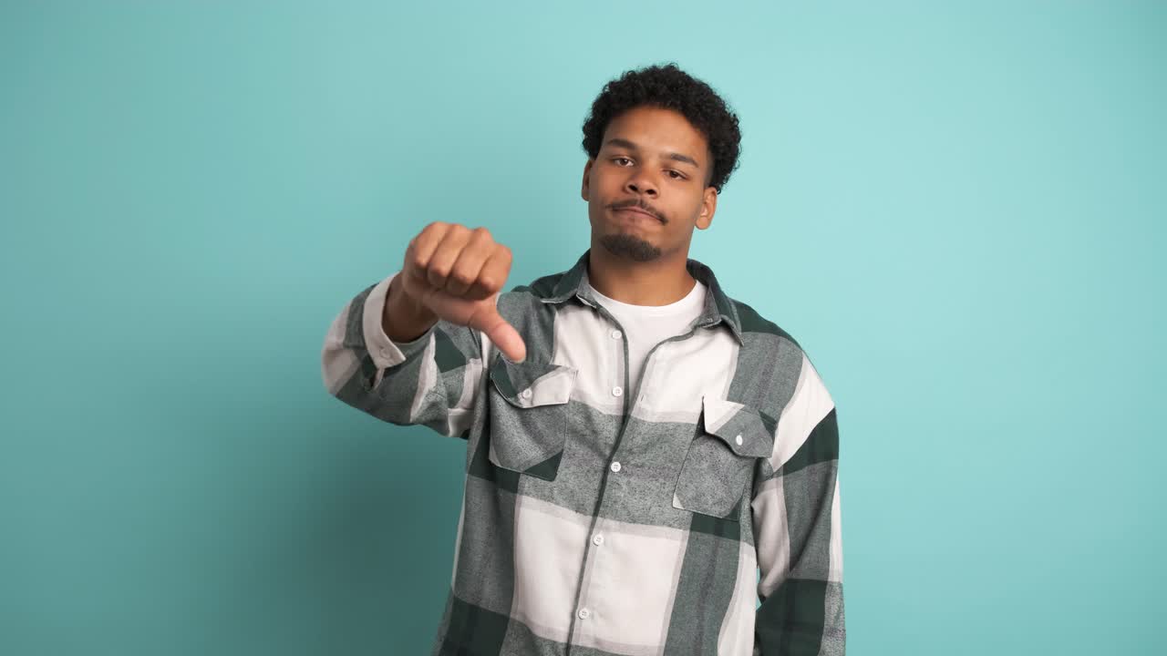 Sad young man showing thumb down in blue studio