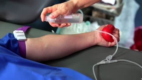 donor's hand is squeezing the red rubber ball for blood inflow. medic sprays the arm with antiseptic. close up.