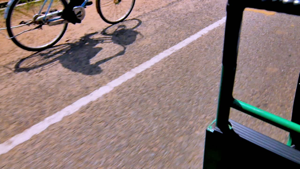 Motion blur of asphalt road captured from green tuk-tuk as cyclist's shadow passes by