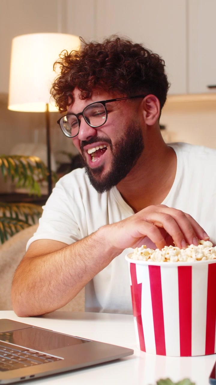 Uomo arabo riproduce un trailer di un film sul laptop, mangia popcorn, ride a voce alta, si gode l'anteprima di notte al chiuso