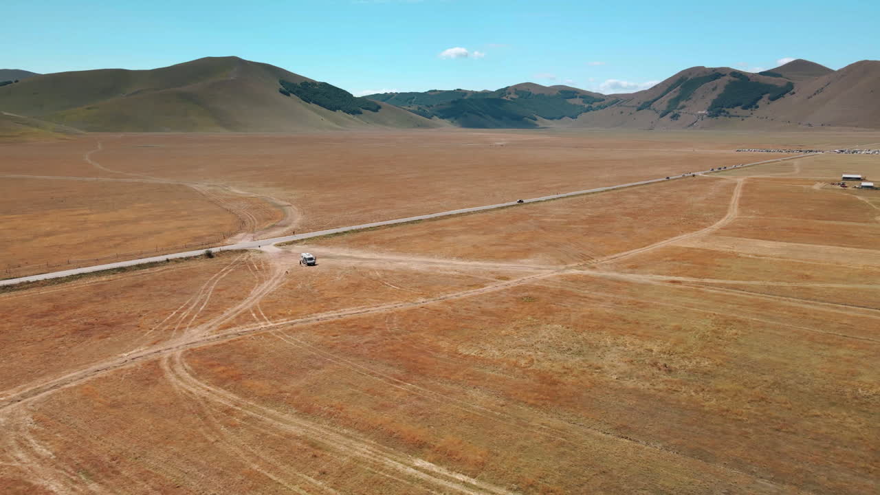 vista aérea de la carretera en medio de piana grande con vistas a la montaña en un día soleado en castelluccio di norcia, toscana, italia