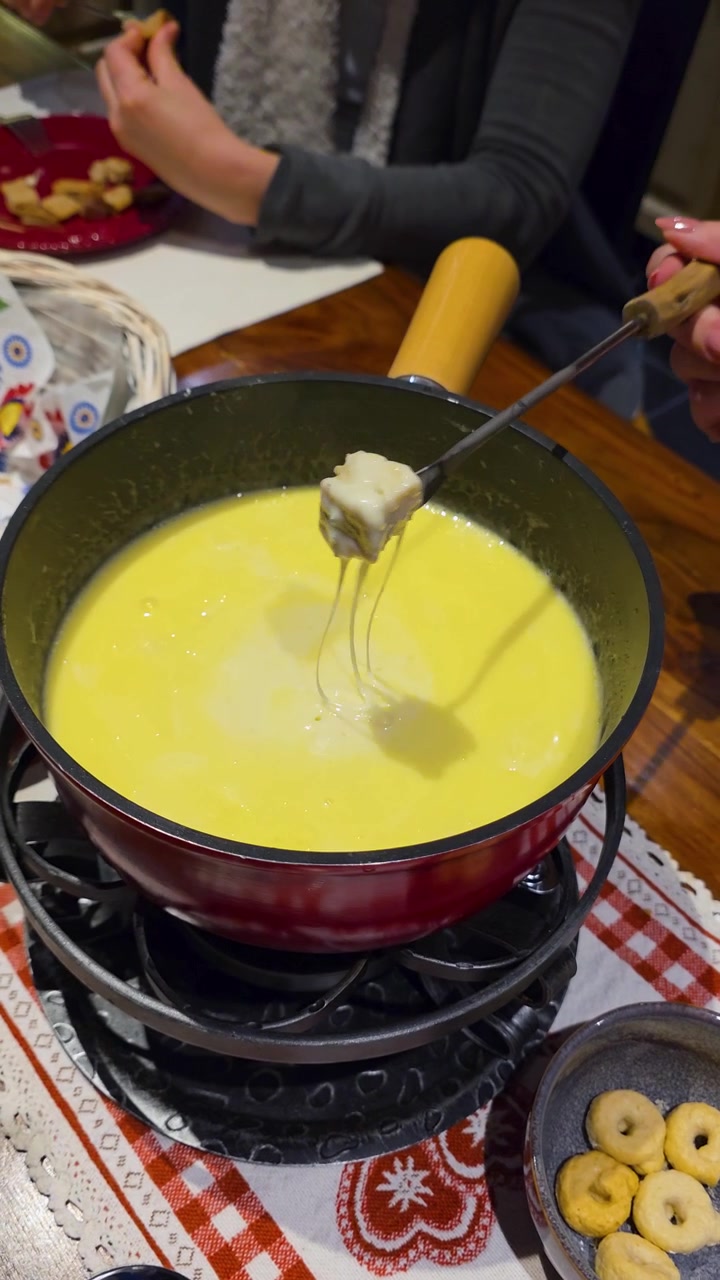 La fondue au fromage suisse bouillonne dans un caquelon domestique tandis que du pain est trempé et remonté.