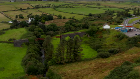 Slide-and-pan-aerial-shot-of-historic-railway-bridge.-Technical-landmark-of-Lispole-viaduct-over-valley-and-stream.-Ireland